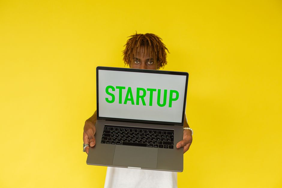 Joven sosteniendo un portátil con la palabra Startup sobre fondo amarillo vibrante
